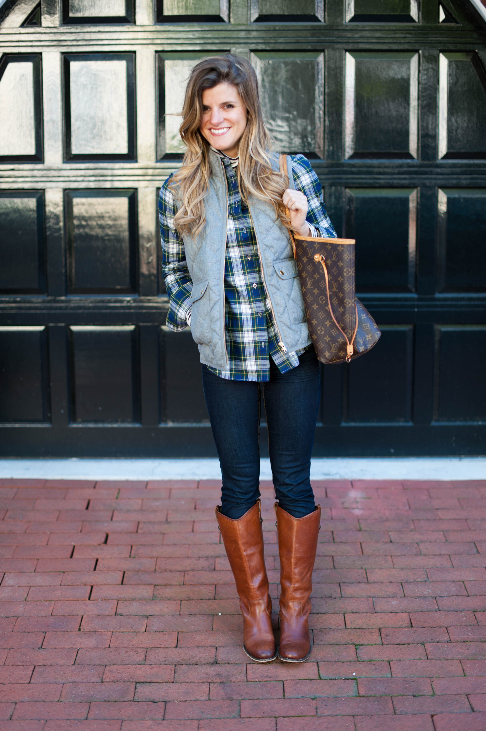 preppy outfit with striped turtleneck and plaid button up and grey puffer vest and riding boots