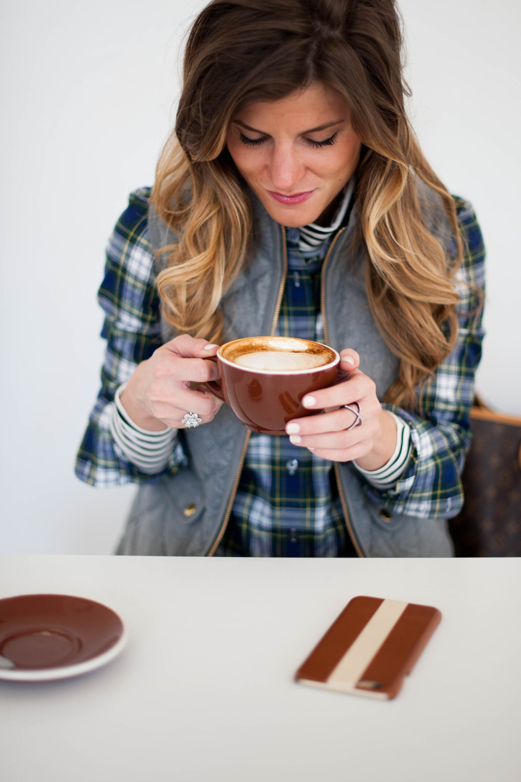 preppy outfit with striped turtleneck and plaid button up and grey puffer vest and pearls and coffee 