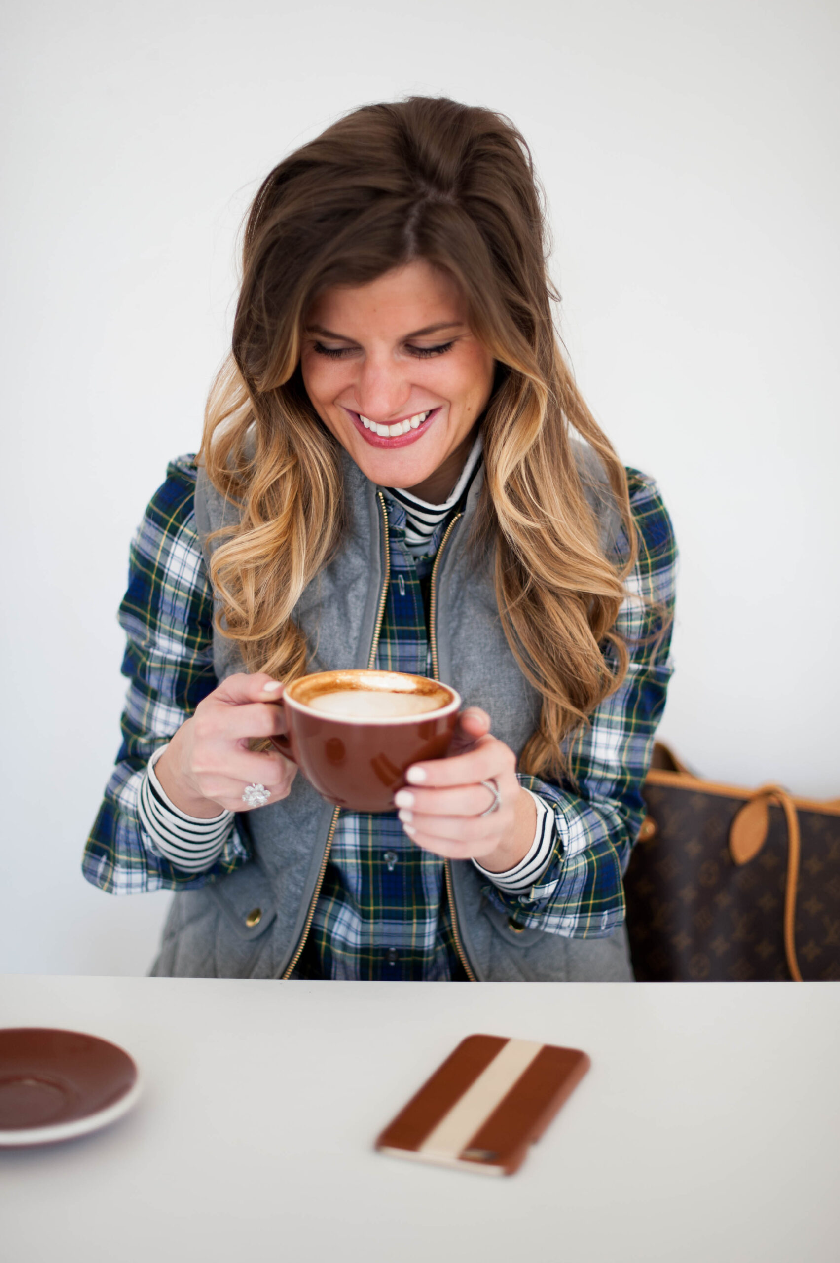 preppy outfit with striped turtleneck and plaid button up and grey puffer vest and pearls and coffee 