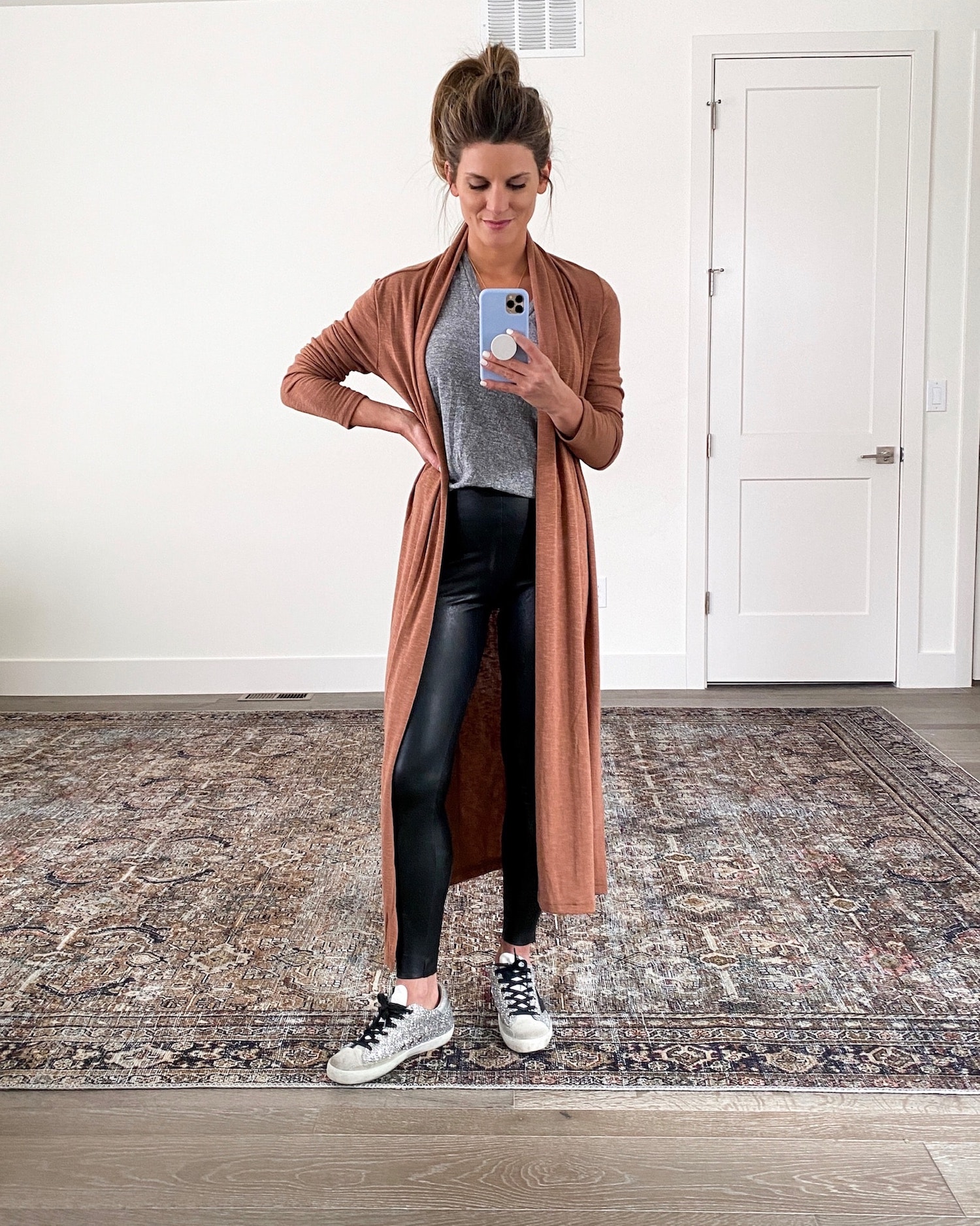 Brighton Keller wearing leather leggings, grey t -shirt, golden goose sneakers and duster