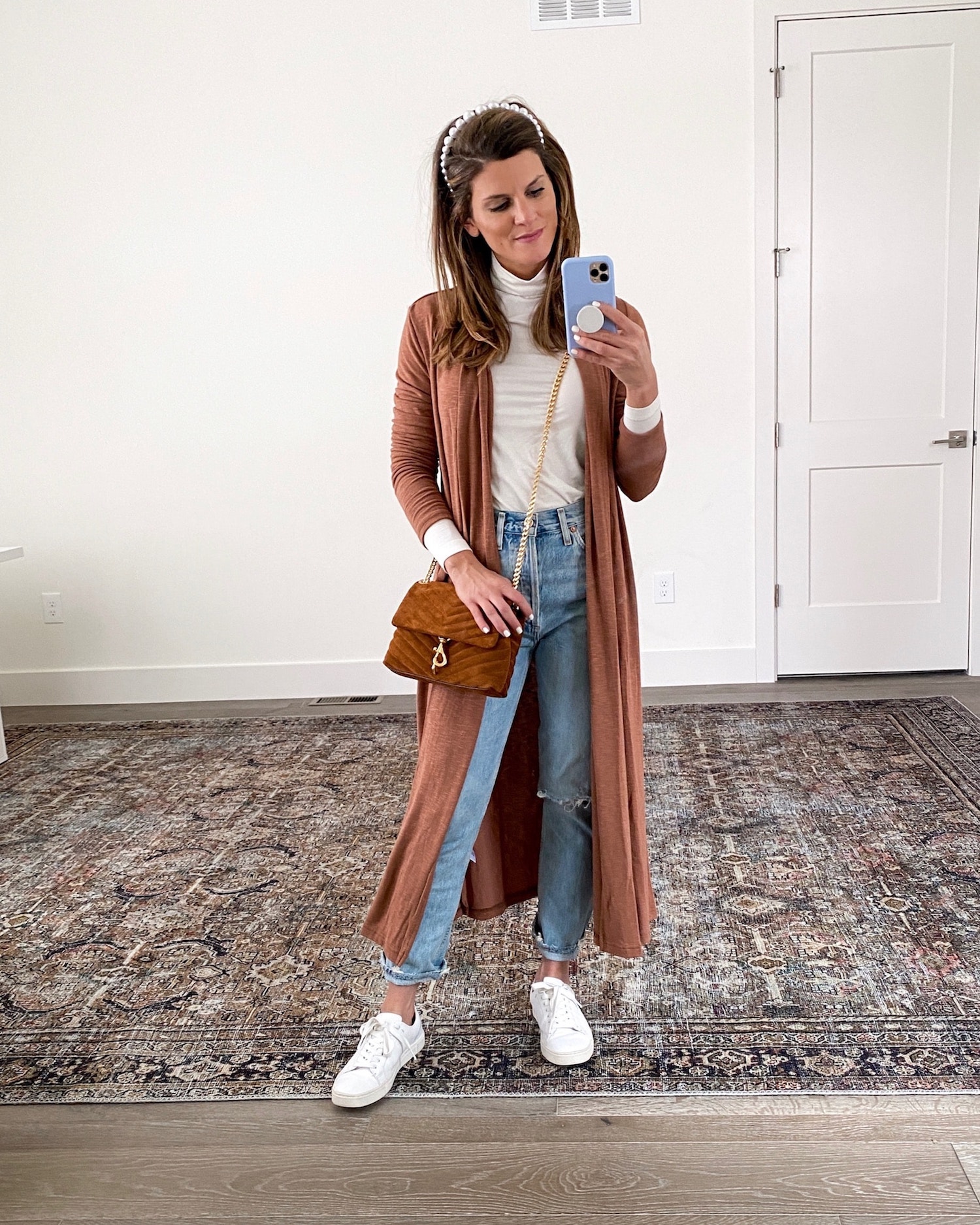 Brighton Keller wearing white turtleneck, light wash jeans, white tennis shoes, duster and pearl headband