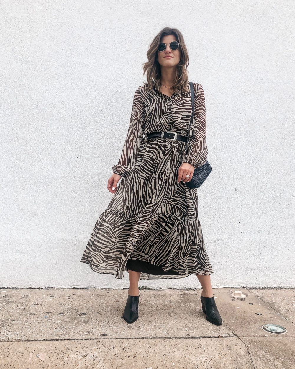 brighton keller wearing animal print dress with mules and belt on white wall