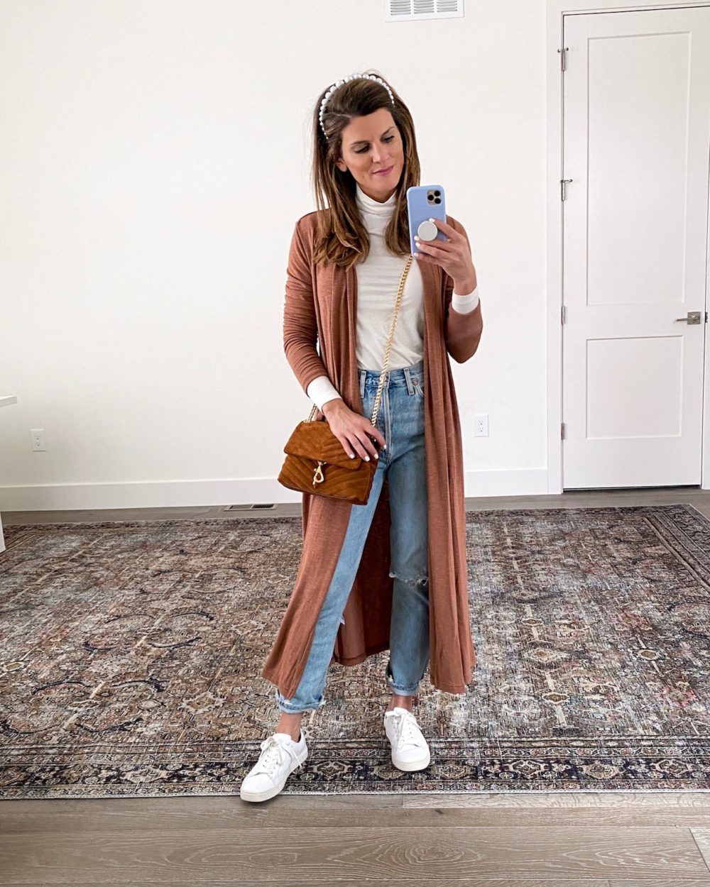 Brighton Keller wearing white turtleneck, rust duster, mom jeans and white sneakers