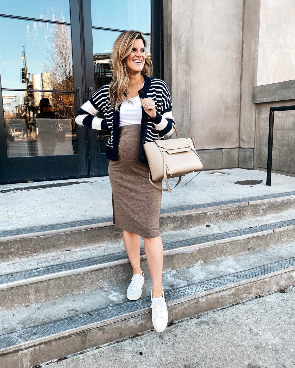 Brighton Butler wearing a tan sweater skirt, white tank, striped cardigan and sneakers, pregnancy style