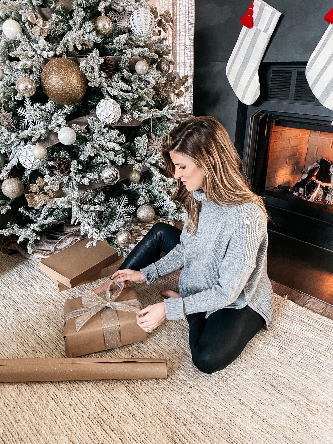 Brighton Butler wrapping gifts under Christmas tree wearing grey turtleneck sweater