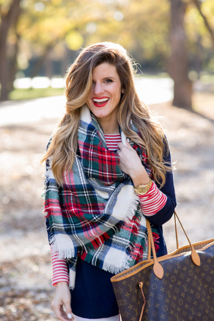 red plaid scarf, navy sweater, red and white striped shirt, white jeans, and tory burch riding boots