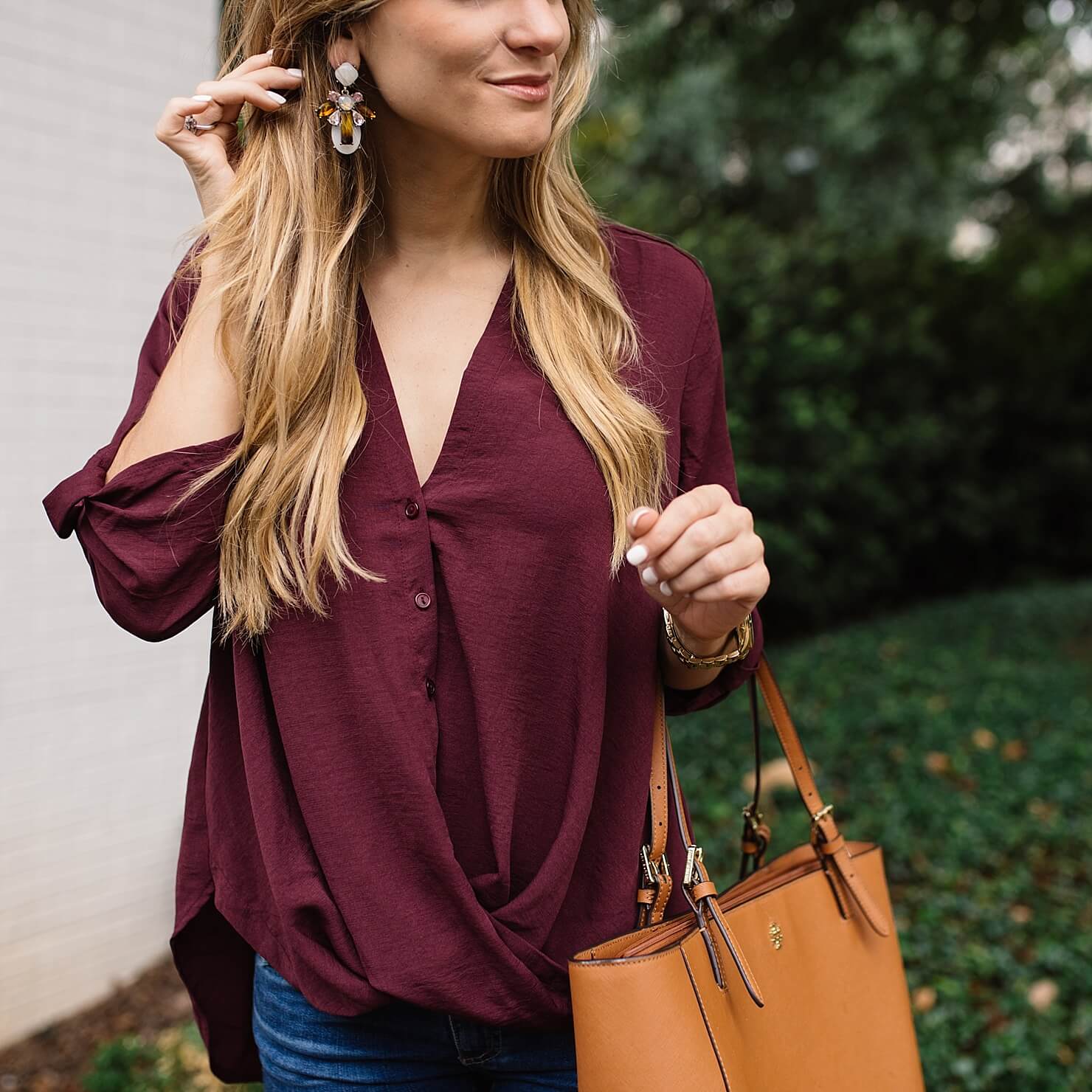 close up shot of burgundy twist front blouse and baublebar earrings 