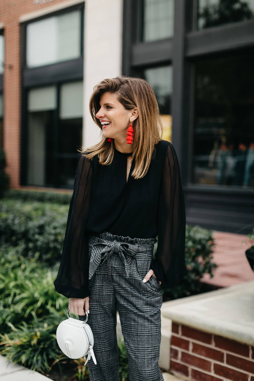 plaid trouser, black blouse, black pumps, and red tassel earrings